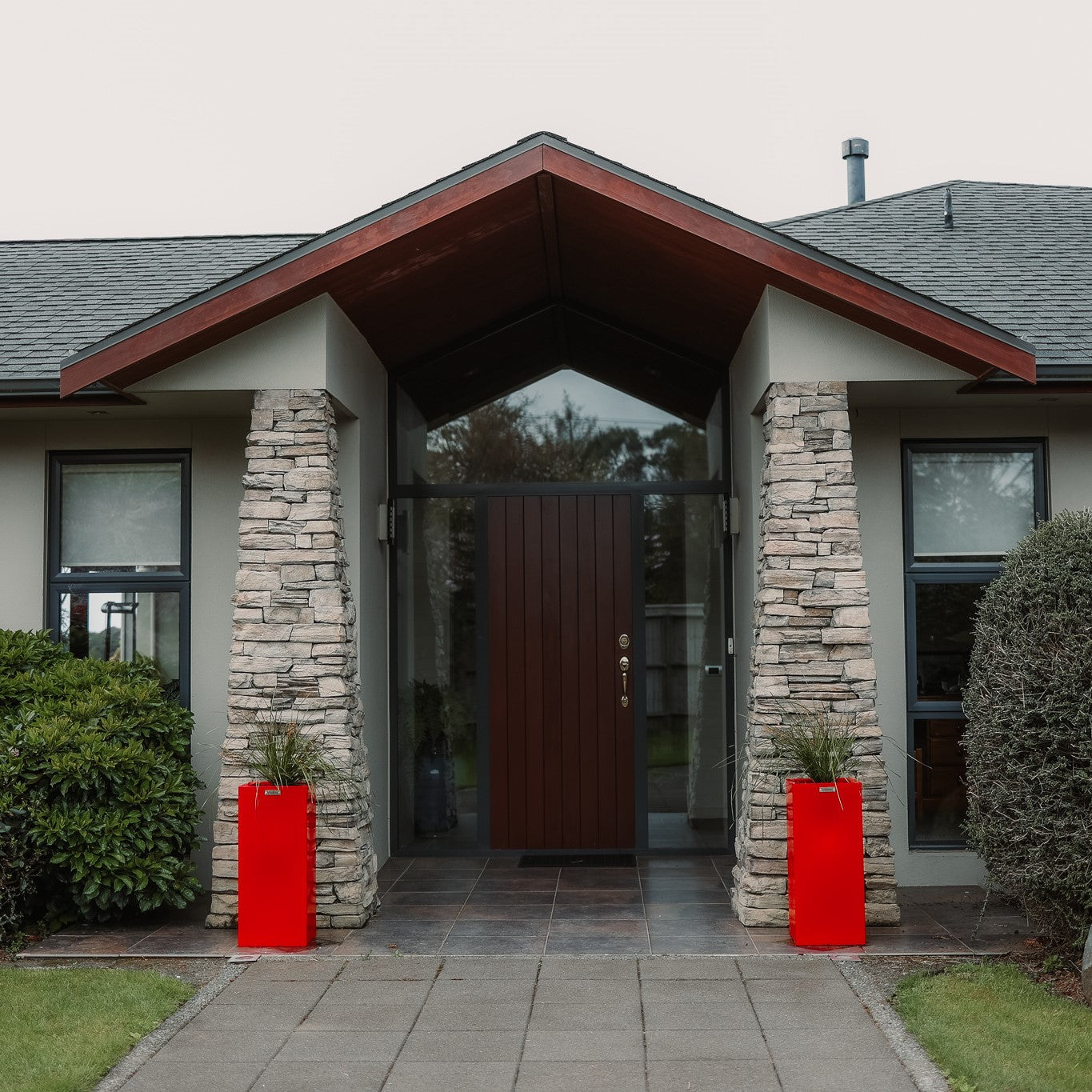 Two cube planter pots either side of a house entrance way in front of stone pillars.