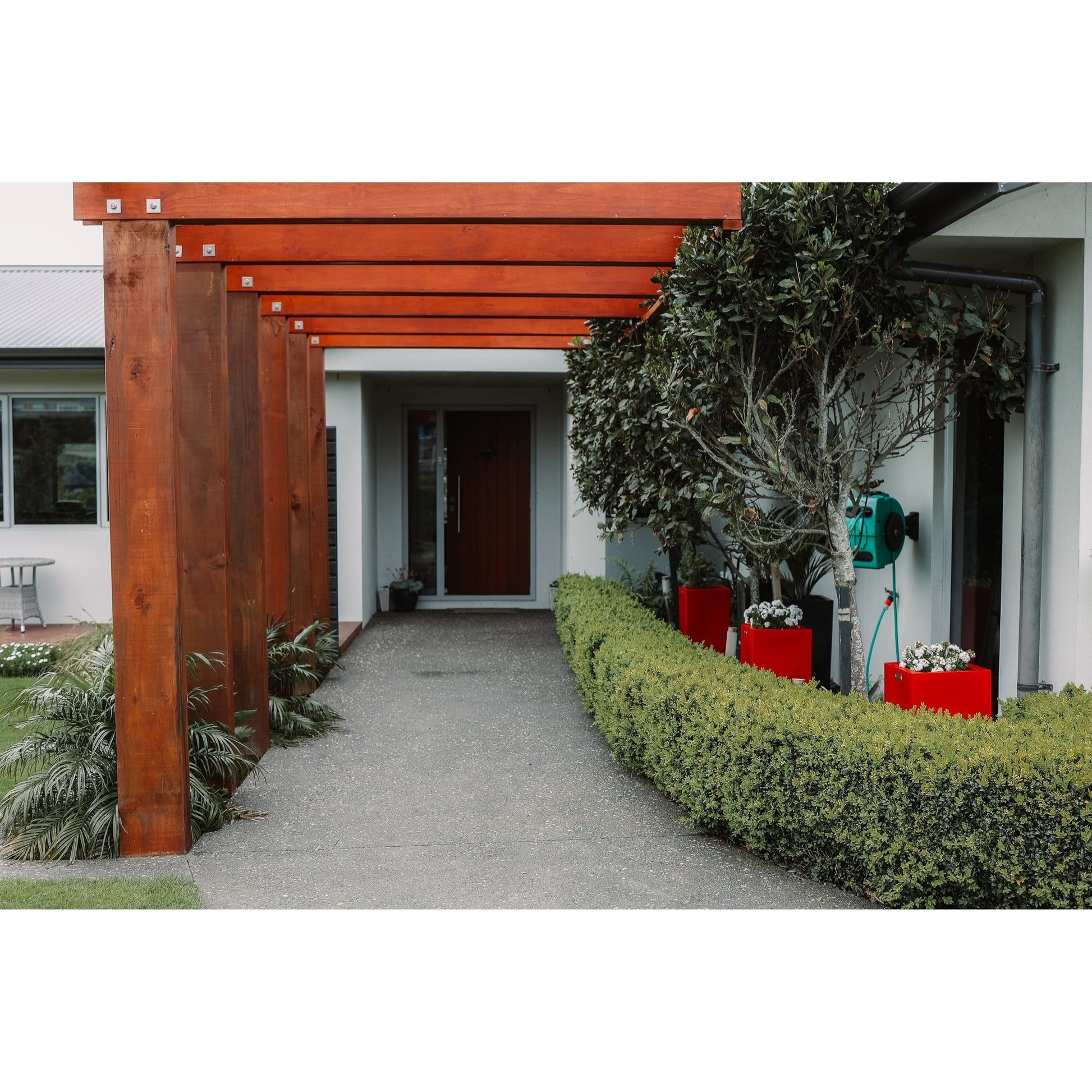 A row of red cube planters in a garden behind a hedge.