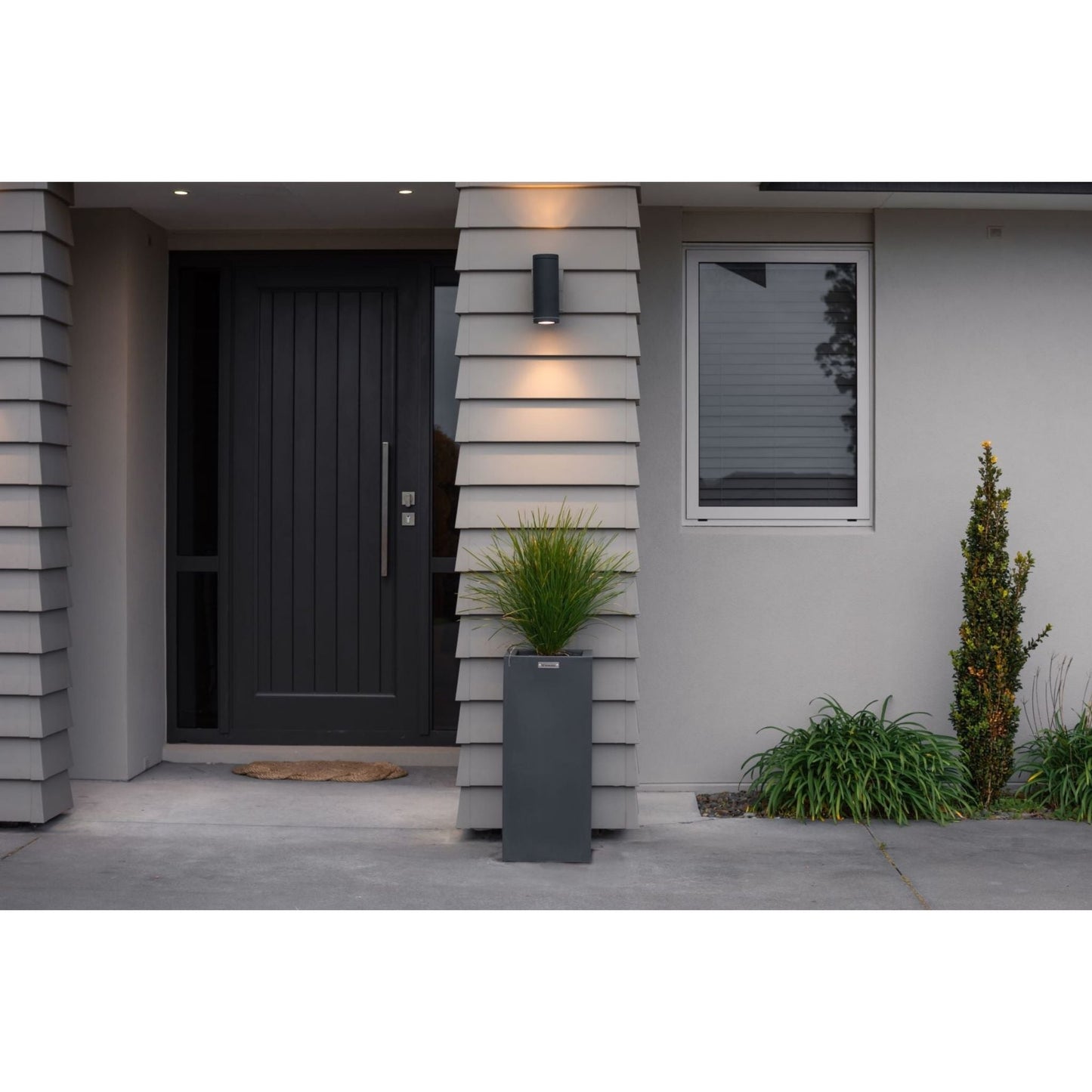 A cube planter pot in a dark grey colour sitting beside a house entranceway.