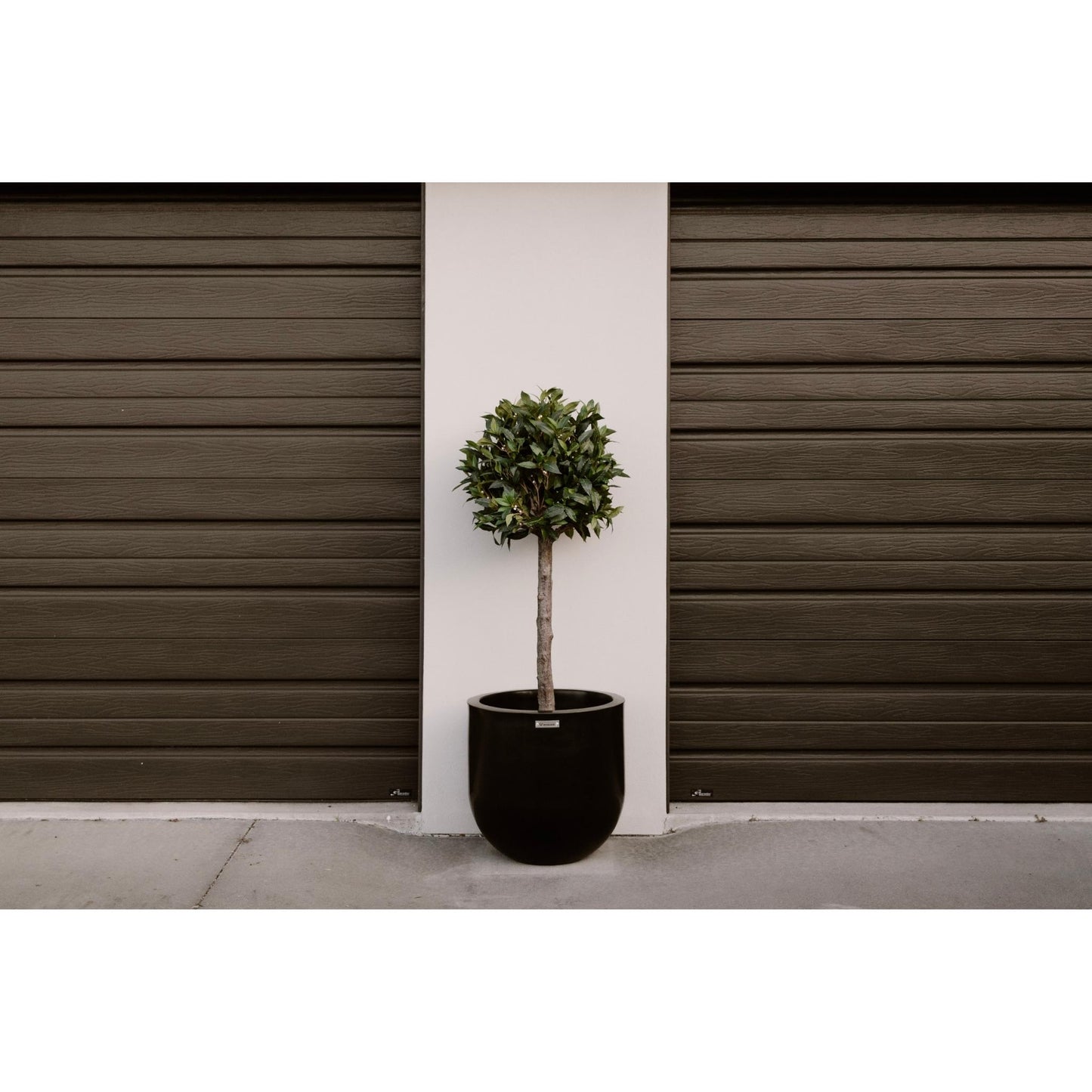 A Modscene planter in black situated between the garage doors of a house.